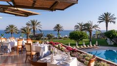 Genießen Sie ein stilvolles Abendessen auf der Terrasse mit Blick auf Palmen, Pool und das weite Meer – perfekt zum Sonnenuntergang.