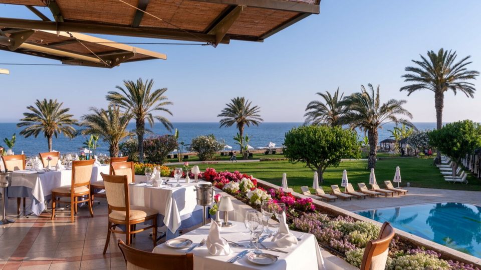 Genießen Sie ein stilvolles Abendessen auf der Terrasse mit Blick auf Palmen, Pool und das weite Meer – perfekt zum Sonnenuntergang.