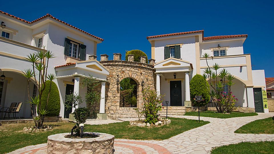 Charmante Hotelanlage im mediterranen Stil mit liebevoll gepflegtem Garten, hellen Fassaden und einem dekorativen Rundbogen aus Naturstein.