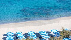 Reihe von blau-weißen Sonnenschirmen an einem feinsandigen Strand mit kristallklarem Wasser in verschiedenen Türkistönen.