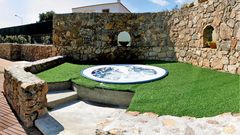 Kleiner Whirlpool im Freien, eingebettet in eine charmante Steinmauer mit rustikalem Flair – umgeben von Kunstrasen und mediterranem Ambiente für entspannte Momente unter freiem Himmel.
