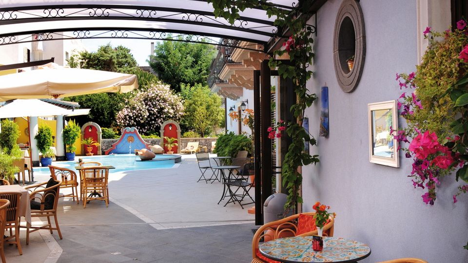 Lipari Hotel Arciduca ©michelangelo int travel, momento Stilvoll gestalteter Innenhof mit kleinem Brunnen, bunten Wanddekorationen, gemütlichen Sitzplätzen und mediterraner Bepflanzung – lebendige Farben und liebevolle Details sorgen für ein einladendes Ambiente.