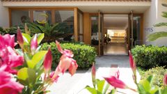 Einladender Hoteleingang mit gepflegter Gartenanlage, blühenden Blumen und offen gestalteter Lobby.