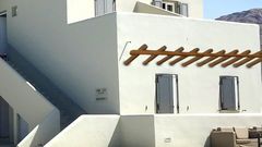Traditionell weißes Gebäude mit typischer kykladischer Architektur und gemütlichem Sitzbereich am glitzernden Pool – perfekter Ort zum Entspannen unter der Sonne Santorins.
