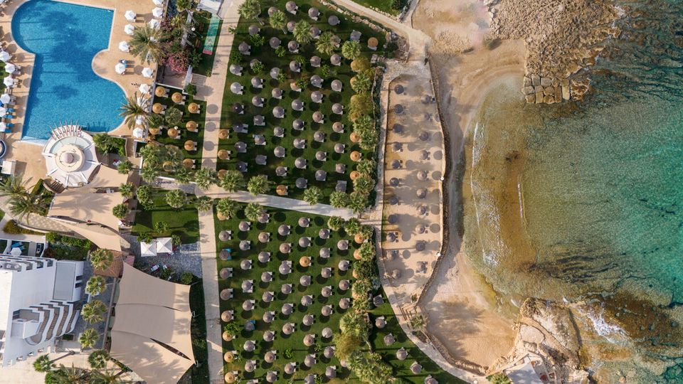 Großzügige Gartenanlage mit Schatten spendenden Palmen und zahlreichen Sonnenschirmen – direkt am feinsandigen Strand und kristallklaren Meer gelegen.