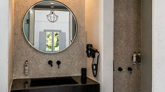 Modernes Bad mit stilvollem Waschbereich, schwarzem Waschbecken, großzügigem Spiegel und begehbarer Dusche mit Regenduschkopf – alles in harmonischen Naturtönen gehalten.