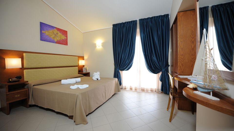 Freundlich eingerichtetes Doppelzimmer mit hellen Farben, gemütlichem Bett und Schreibtisch – ideal zum Entspannen nach einem Urlaubstag.