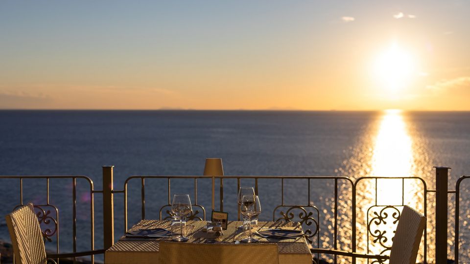 Romantisch gedeckter Tisch für zwei mit Meerblick bei Sonnenuntergang – Weingläser, Besteck und warme Lichtstimmung.