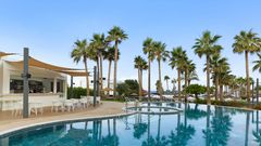 Stilvolle Poolbar mit bequemen Sitzmöglichkeiten – umgeben von Palmen und nur wenige Schritte vom Strand entfernt.